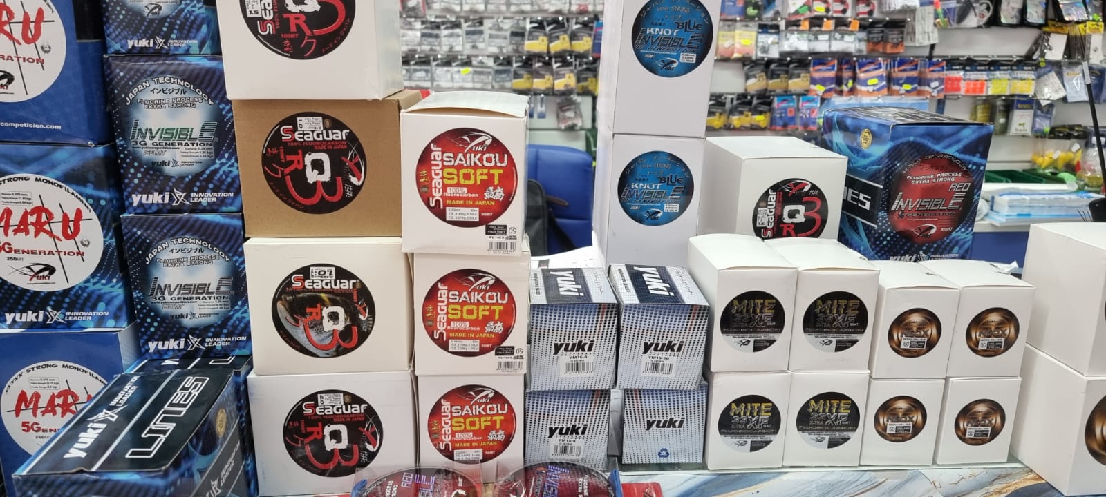Scatole di filo da pesca Seaguar R18, Saikou Soft e Yuki Invisible impilate davanti a espositori di minuteria